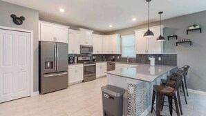 A modern kitchen with white cabinets, stainless steel appliances, a central island with bar stools, and pendant lighting.