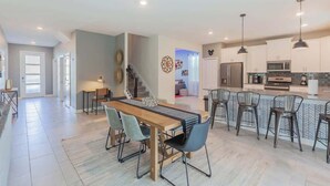 A spacious living area with a wooden dining table, multiple chairs, and a kitchen area with modern appliances and bar stools.