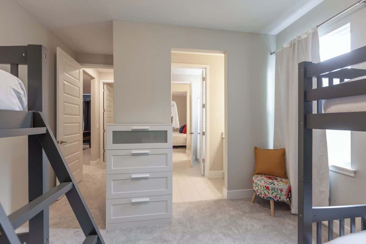A bedroom with bunk beds, a wardrobe, a small table, and a chair.