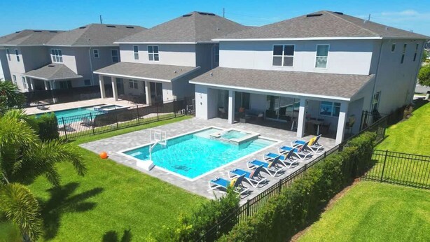 Une maison à deux étages avec une piscine et des chaises longues.