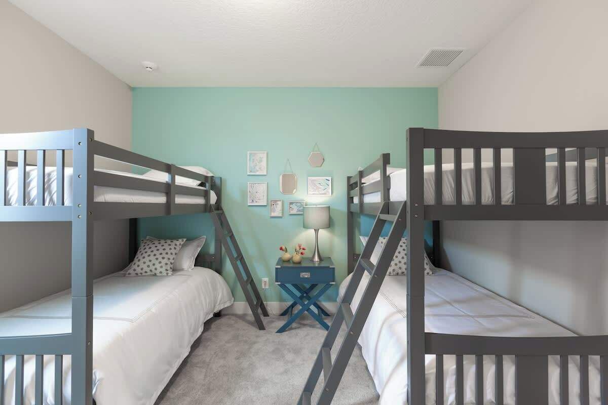 Habitación con literas, una pared verde azulada, una mesita con lámpara y cuadros en la pared.