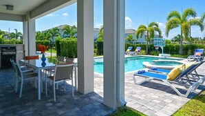 Ein überdachter Außenbereich mit Pool, Liegestühlen und einem Tisch mit Stühlen.