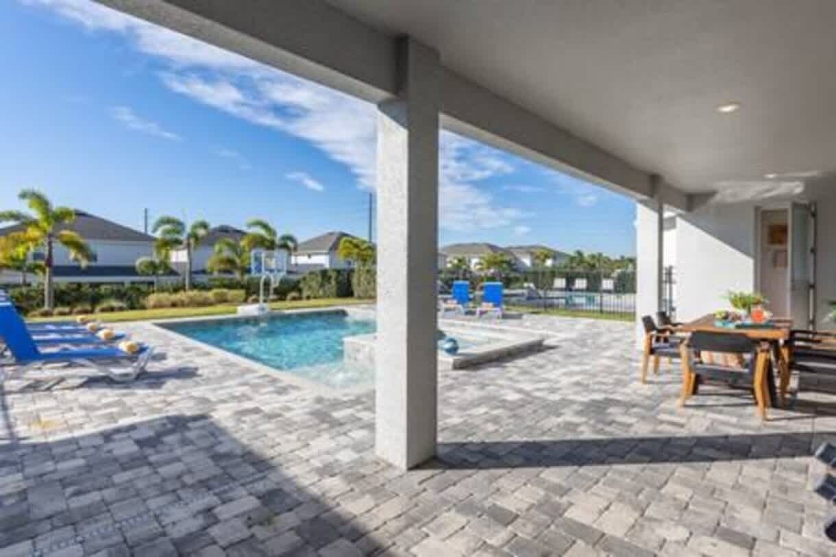 A covered outdoor area with a pool, lounge chairs, and a table with chairs.