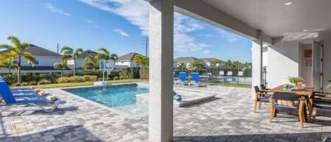 A covered outdoor area with a pool, lounge chairs, and a table with chairs.