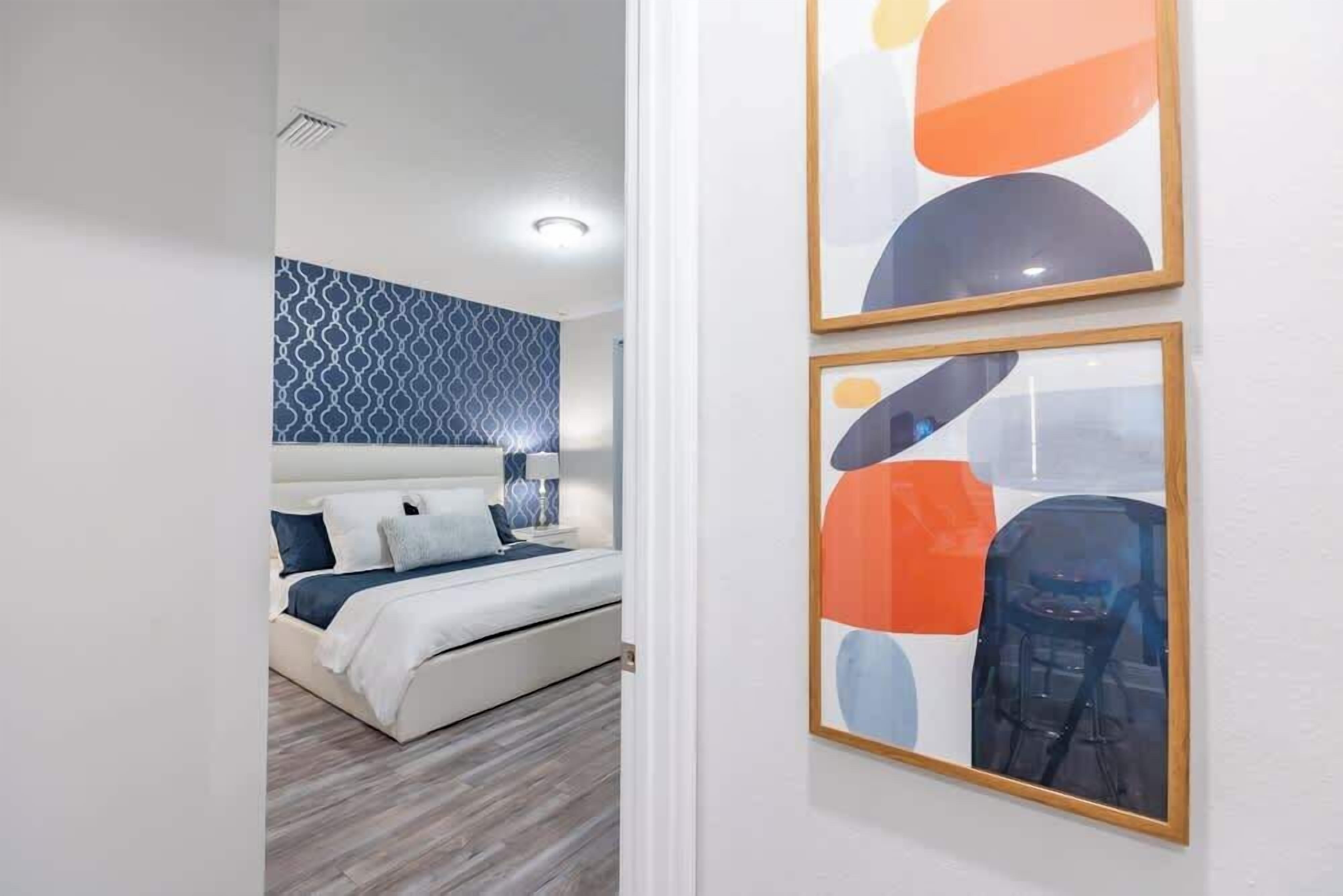 Une chambre moderne avec un mur orné d’un motif, un lit recouvert de linge de lit blanc et deux tableaux abstraits accrochés au mur.