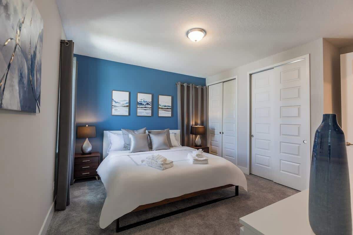 A hotel room with a large bed, two bedside tables with lamps, a white door, and a blue accent wall.