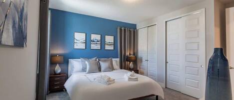A hotel room with a large bed, two bedside tables with lamps, a white door, and a blue accent wall.