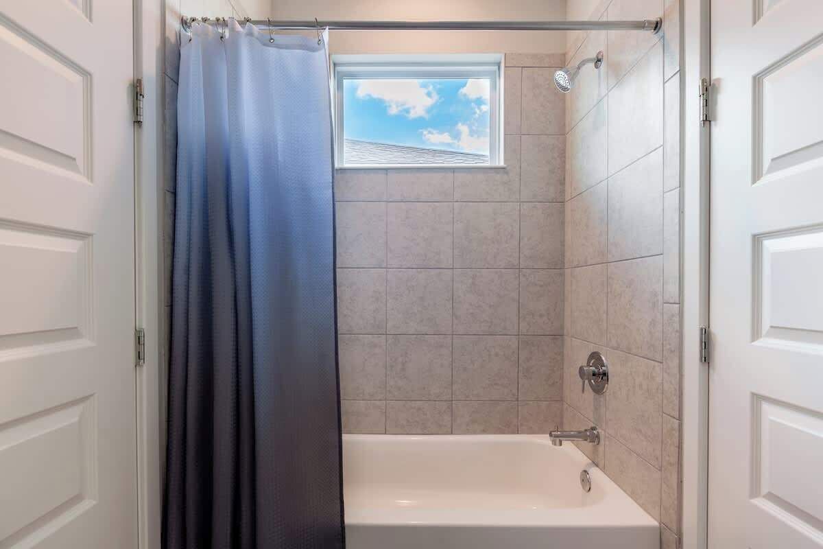 Une douche avec fenêtre, une baignoire et des murs carrelés.