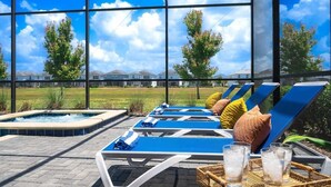 Un área junto a la piscina con sillones de descanso, un jacuzzi y vistas a casas al fondo.