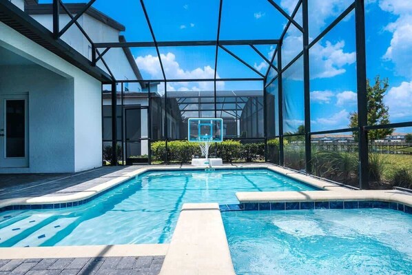 A swimming pool with a glass enclosure, surrounded by a white building and greenery.