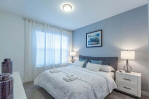 Ein Hotelzimmer mit einem großen Bett, zwei Nachttischen, einem Fenster mit Vorhängen und einem gerahmten Bild an der Wand.