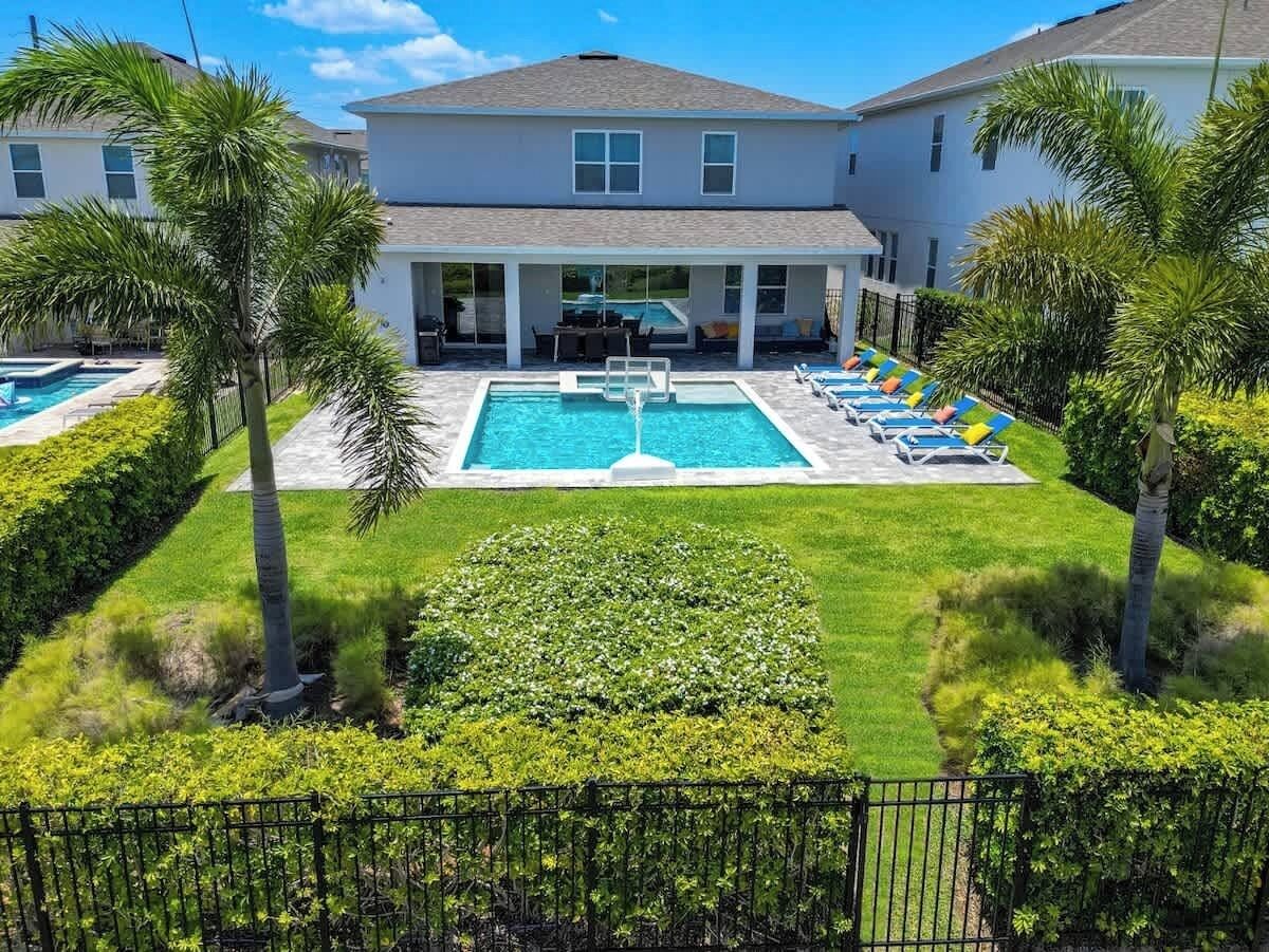 Propiedad residencial con piscina, sillas de descanso y palmeras.