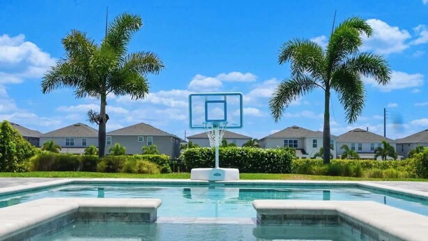 Ein Schwimmbad mit Basketballkorb, umgeben von Palmen und Häusern.