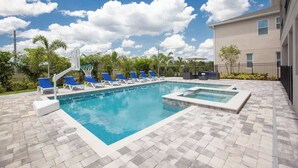 Une piscine avec des chaises longues, un panier de basketball et un bâtiment en arrière-plan.