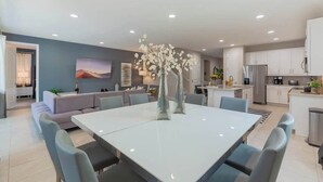 Un espace repas moderne comprenant une grande table et des chaises, un canapé et un vase décoratif.