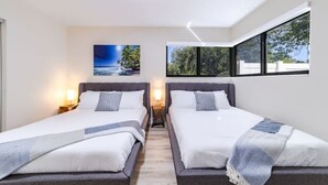 Ein Hotelzimmer mit zwei Betten, jeweils mit Nachttisch und Lampe, einem großen Fenster mit Blick und einem Bild an der Wand.