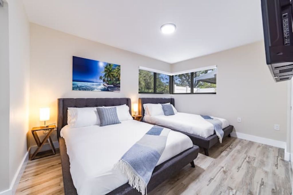 A hotel room with two beds, a large window, and a painting on the wall.
