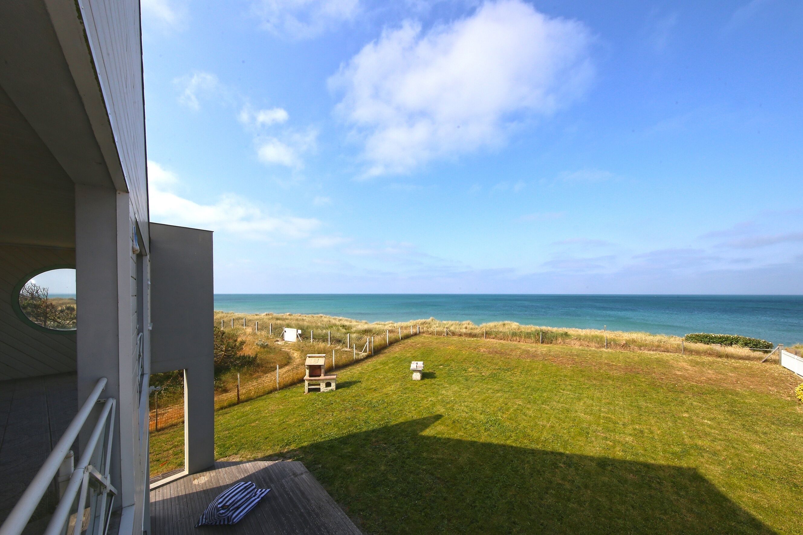 A balcony with a view of the ocean and a grassy area with a fence.