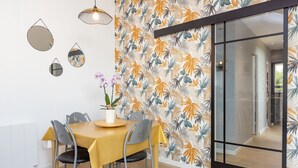 Comedor con una mesa preparada para cuatro personas, una planta en maceta y una pared con estampado de hojas tropicales.