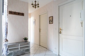 Un pasillo con un banco de madera, una planta en maceta, un candelabro y una puerta blanca.