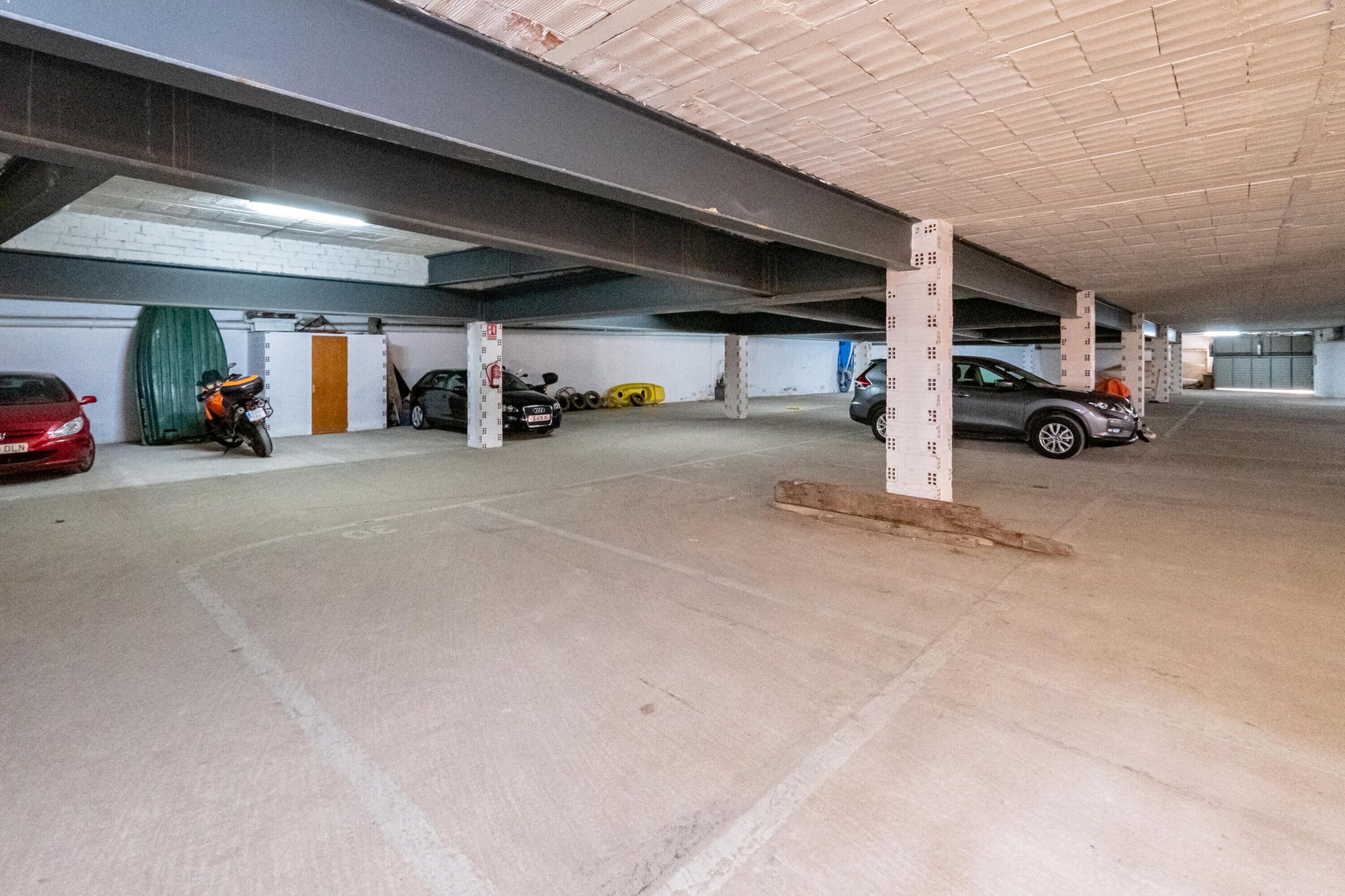 A multi-level parking garage with concrete floors and columns, featuring several parked cars and a motorcycle.