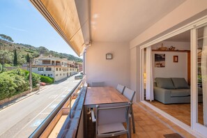 A balcony with a wooden table and chairs, a sofa, and a view of a street and buildings.