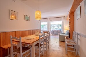 A dining area with a wooden table and white chairs, a hanging light fixture, and a view to an outdoor seating area.