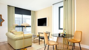 Ein modernes Wohnzimmer mit einer Couch, zwei Sesseln, einem Couchtisch, einem Fernseher und einem Esstisch mit goldener Basis.