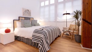 Un dormitorio con una cama, mesitas de noche, una lámpara, una silla y una planta en maceta.