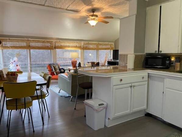 A modern kitchen with white cabinets, a microwave, and a dining area with yellow chairs and a table.