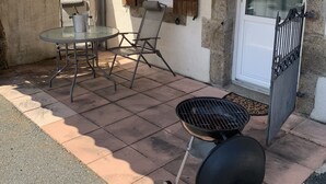 Eine Terrass mit Tisch und Stühlen, einem Grill und einer Tür mit Fenster.