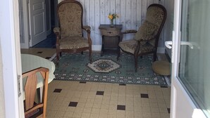 Ein Zimmer mit zwei Holzstühlen, einem kleinen Tisch mit Blumenvase und einem gemusterten Teppich auf Fliesenboden.
