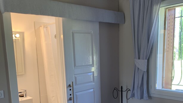 Ein Schlafzimmer mit Bett, Handtüchern, einer Tür, einem Fenster und Blick auf ein Badezimmer.