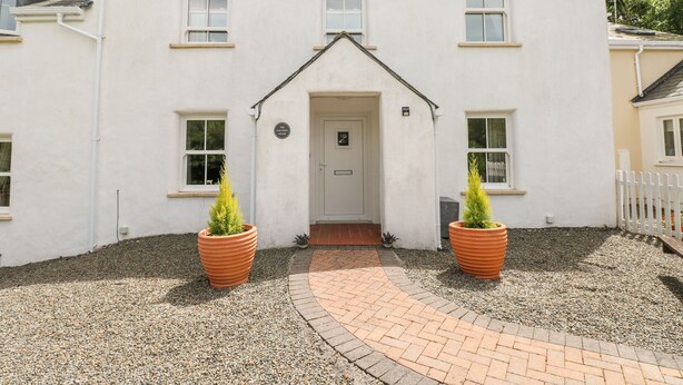 A two-story white building with a central entrance, flanked by two large terracotta planters. - The Old Farm House (Tenby)