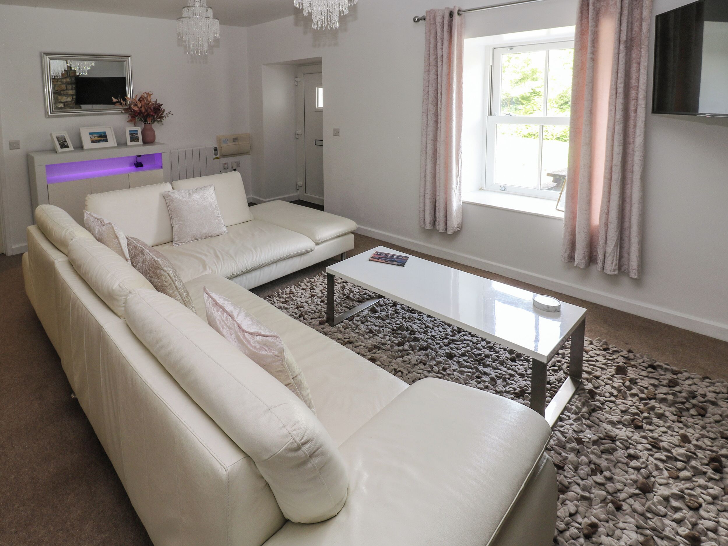 Un salon moderne avec un canapé blanc, une table basse en verre et une grande fenêtre agrémentée de rideaux.