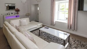 A modern living room with a white sofa, a glass coffee table, and a large window with curtains. - The Old Farm House (Tenby)