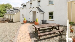 A white building with a paved courtyard, a wooden bench, and potted plants. - The Old Farm House (Tenby)