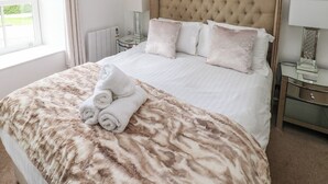 A neatly made bed with a fluffy beige blanket, a set of rolled towels, and two bedside tables with lamps. - The Old Farm House (Tenby)