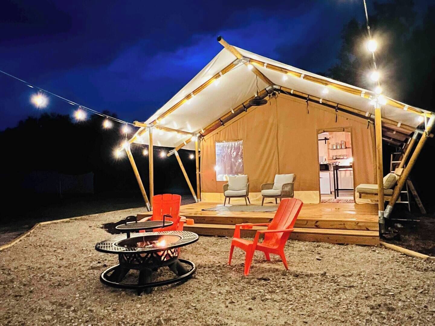 A tent with a covered porch, two chairs, a small table, and a fire pit.