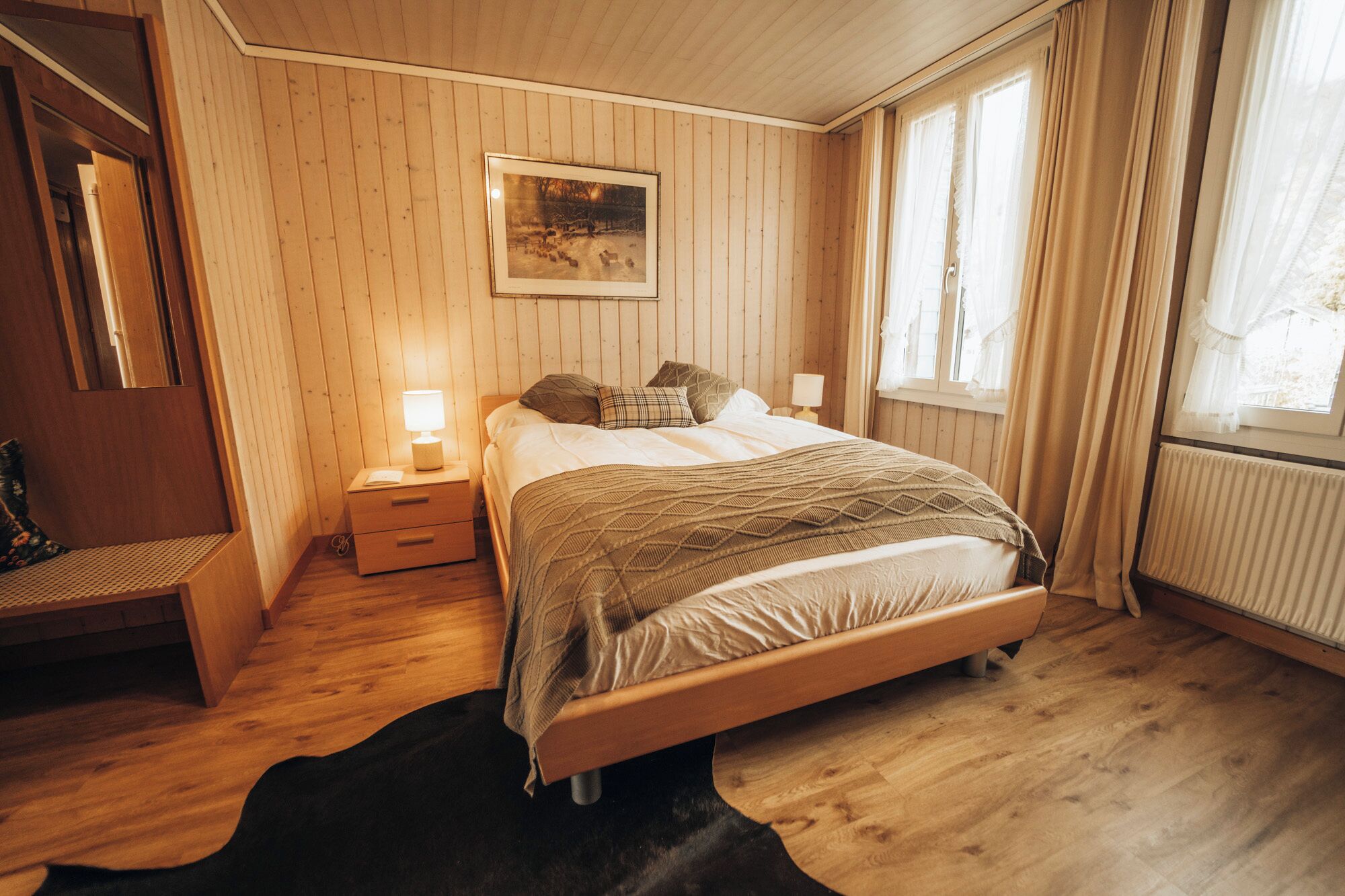 A wooden-paneled bedroom with a bed, bedside lamps, a bench, and a framed picture on the wall.