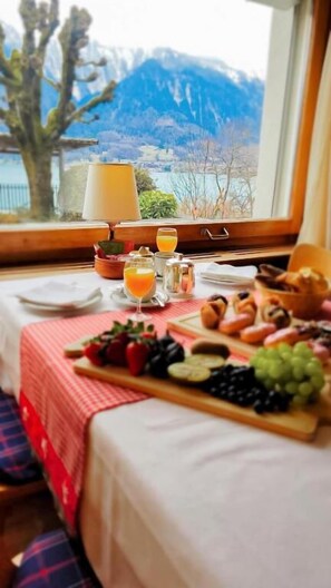 Una mesa junto a una ventana con vistas a la montaña, con un despliegue de frutas, zumo de naranja y pastelería.