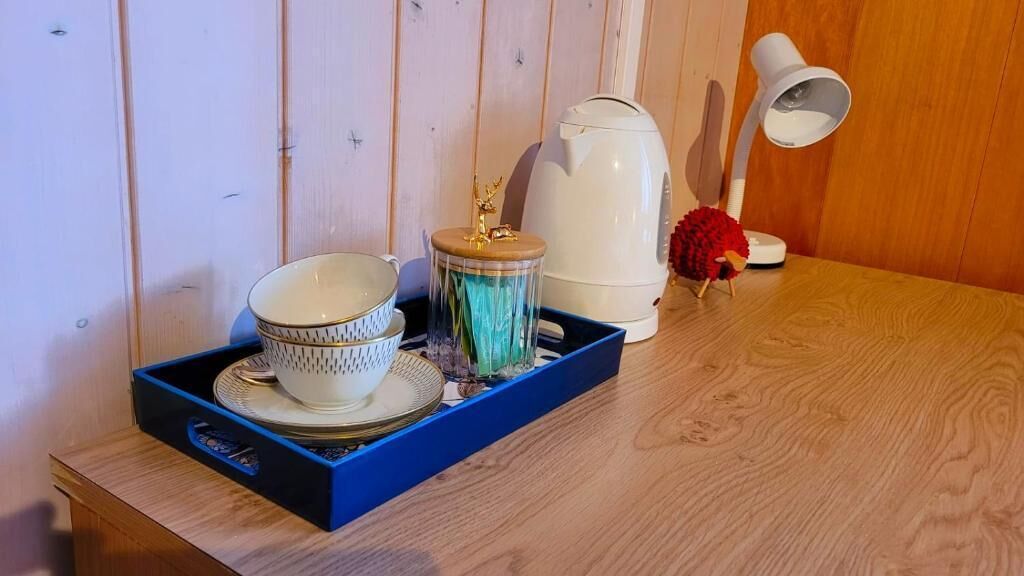 A wooden table with a blue tray holding a white teapot, a red decorative item, and a white lamp.