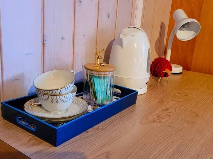 A wooden table with a blue tray holding a white teapot, a red decorative item, and a white lamp.