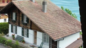 Una cabaña tradicional con techo inclinado, una chimenea y vistas a un lago y montañas.