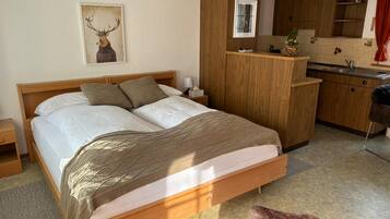 Quarto com cama de madeira, mesa de cabeceira, cozinha com armários de madeira, janela e quadro de veado fixado na parede.