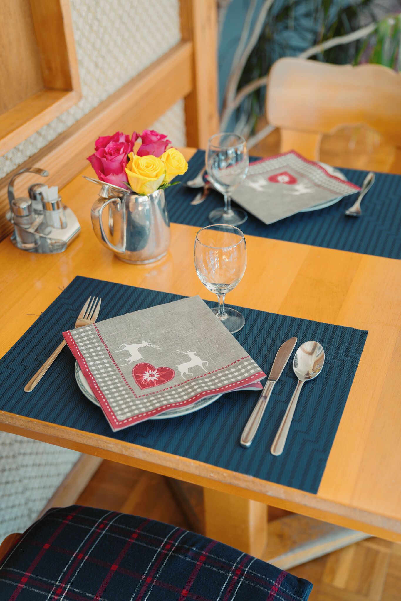 A dining table set with a checkered tablecloth, a vase of flowers, and cutlery.