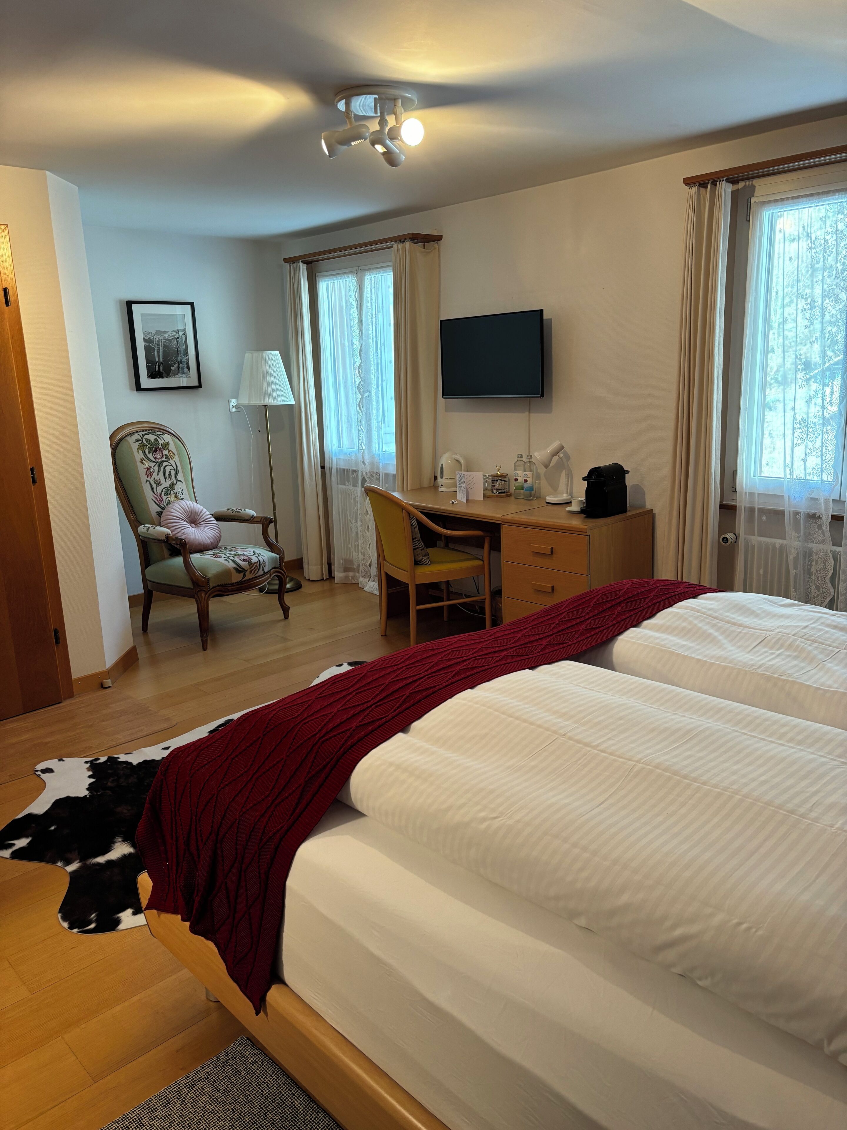 A hotel room with two beds, a desk, a chair, a television, and a window with curtains.