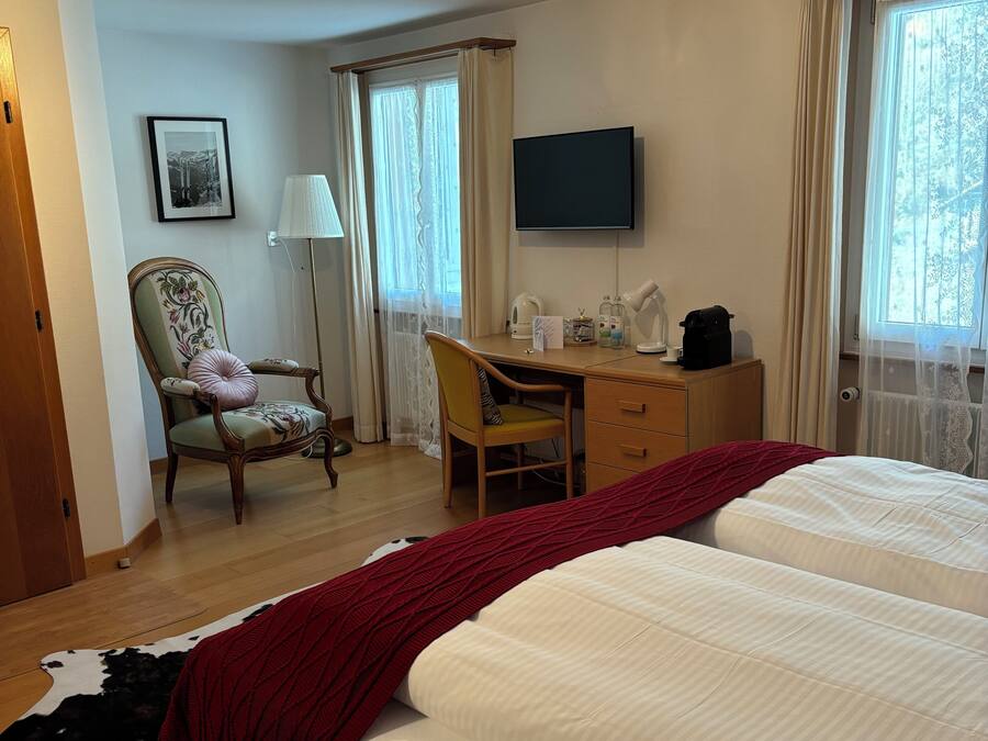 A hotel room with two beds, a desk, a chair, a television, and a window with curtains.
