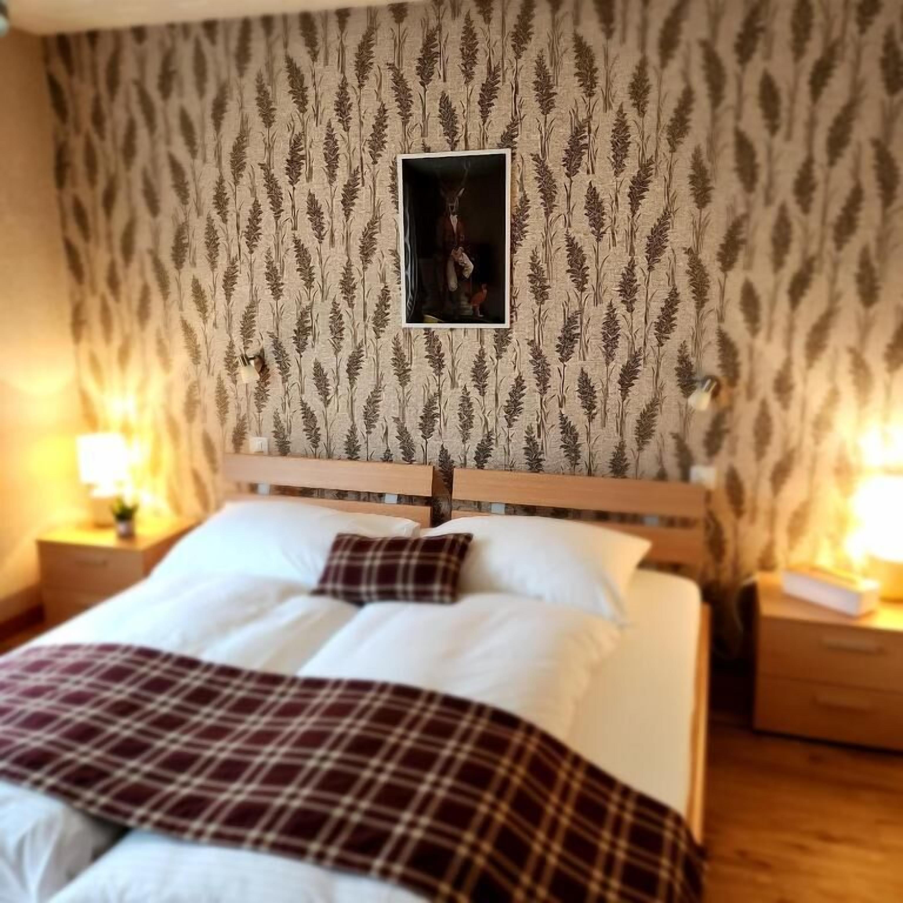 Una cama bien hecha con ropa de cama blanca y escocesa, cabecera de madera y un papel tapiz estampado con una imagen enmarcada en el centro.