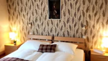 Una cama bien hecha con ropa de cama blanca y escocesa, cabecera de madera y un papel tapiz estampado con una imagen enmarcada en el centro.